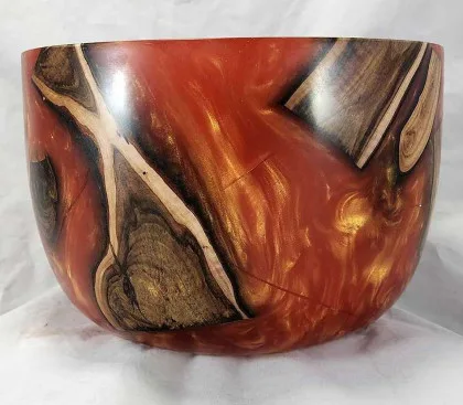 Red-orange epoxy bowl with suspended wood inclusions and glossy finish.